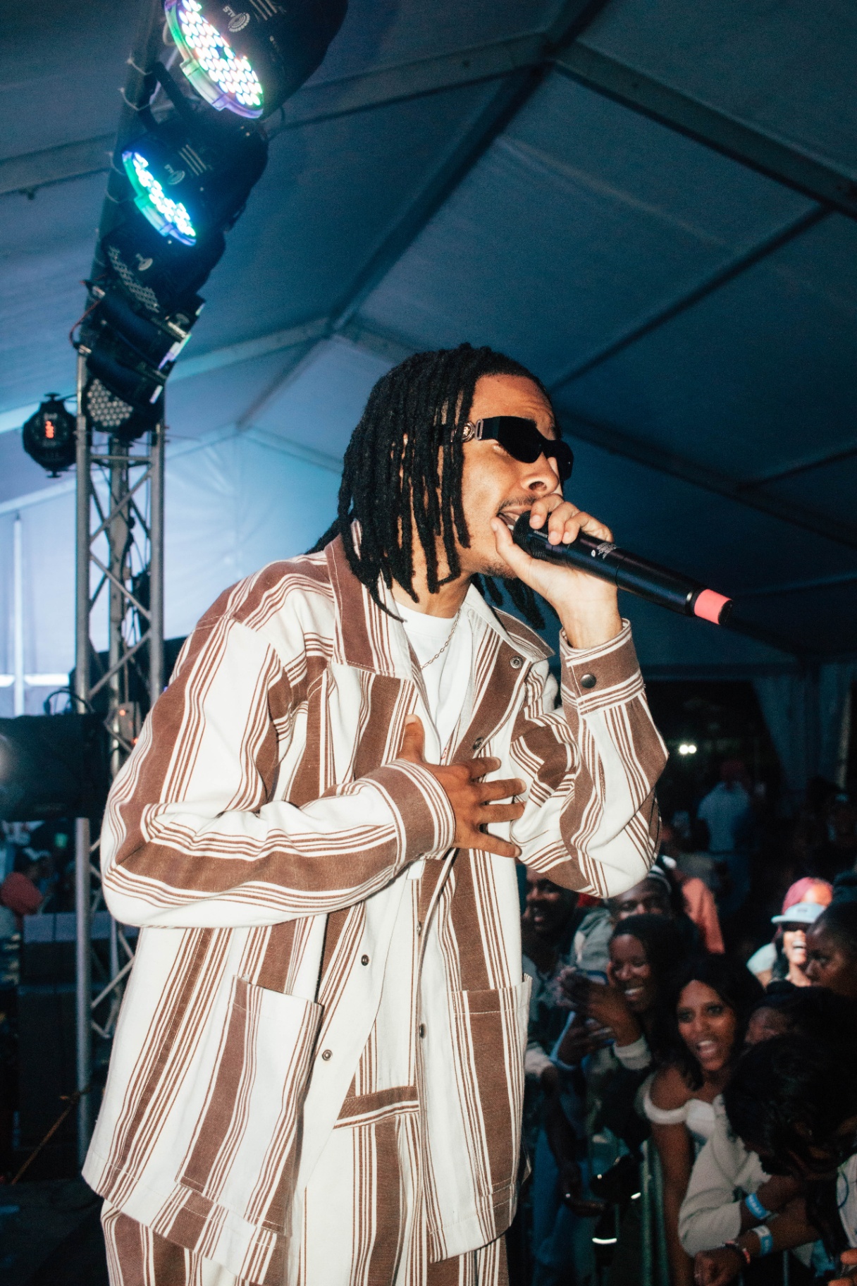Artist on stage holding mic, hand on chest under stage lights