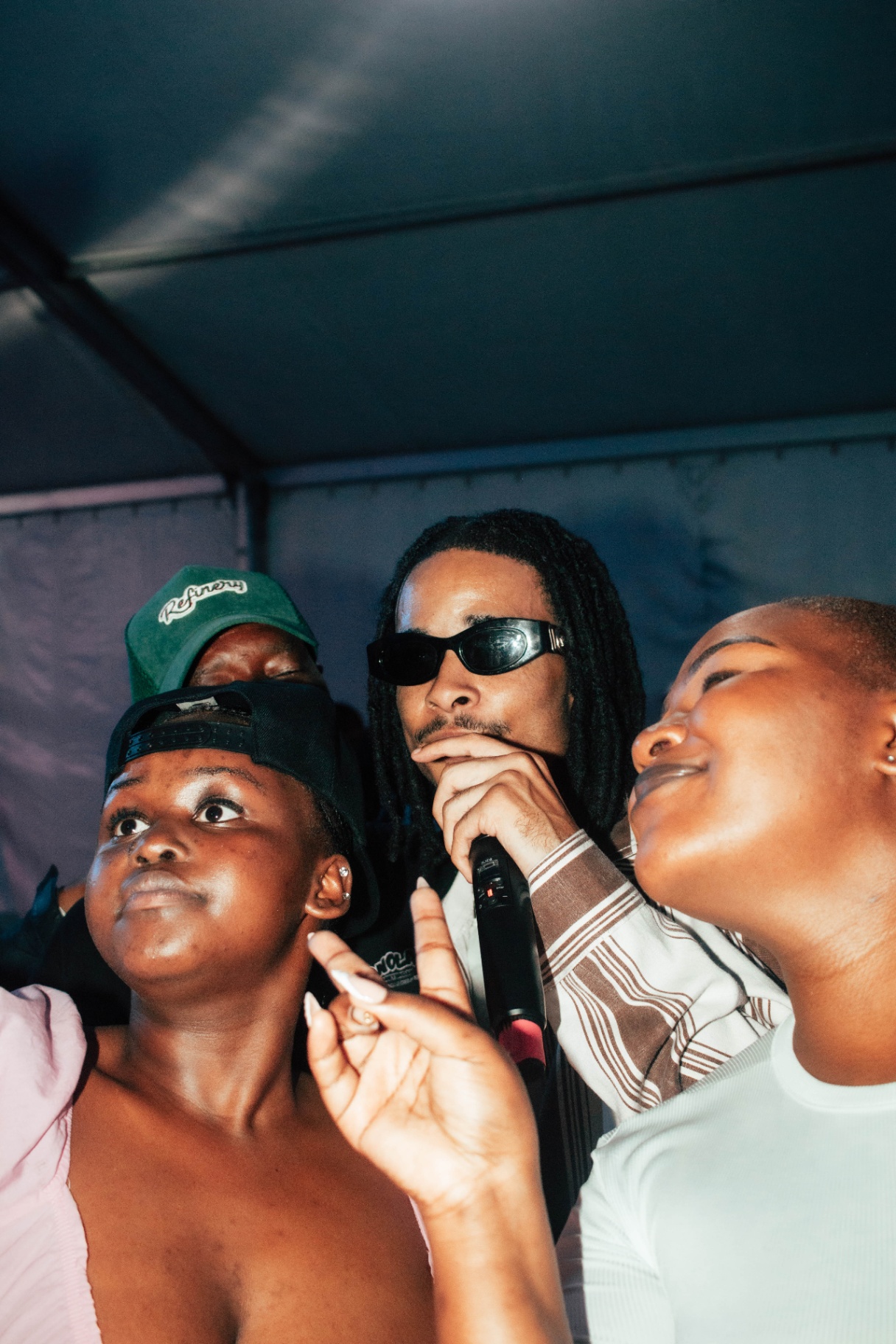 Artist in sunglasses surrounded by fans under tent lights